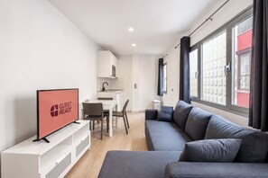 A modern living room with a grey sofa, a dining area with a white table and chairs, and a kitchen in the background. - GuestReady - Artiles Loft Canteras Balcony (Las Palmas de Gran Canaria)