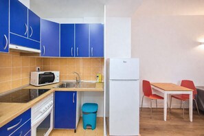 A compact kitchen with blue cabinets, a white refrigerator, a microwave, a sink, and a small dining area with a table and chairs. - GuestReady - Rosamar 302 P (Las Palmas de Gran Canaria)
