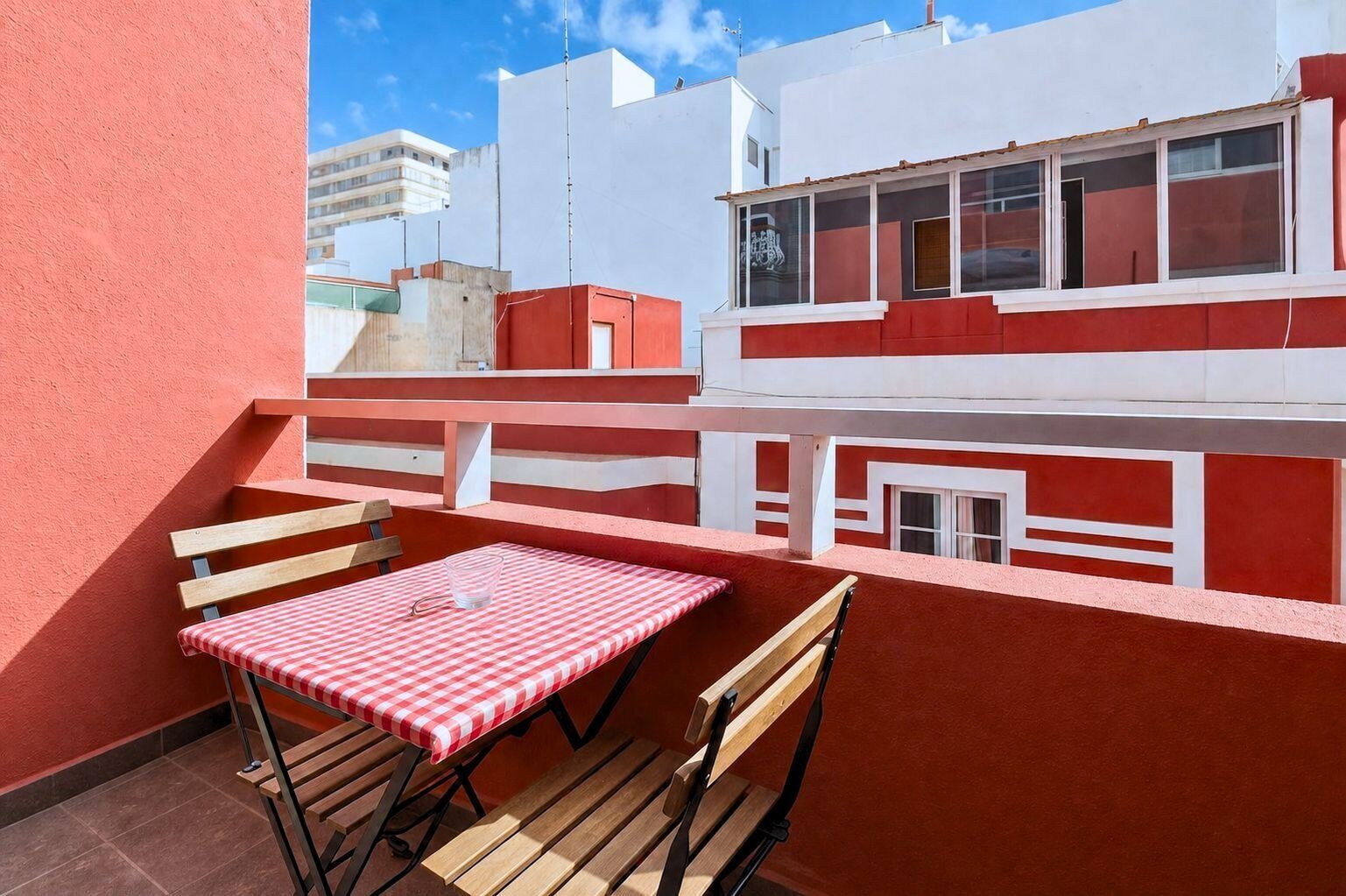 A red and white building with a balcony, a table with a checkered tablecloth, and wooden chairs.