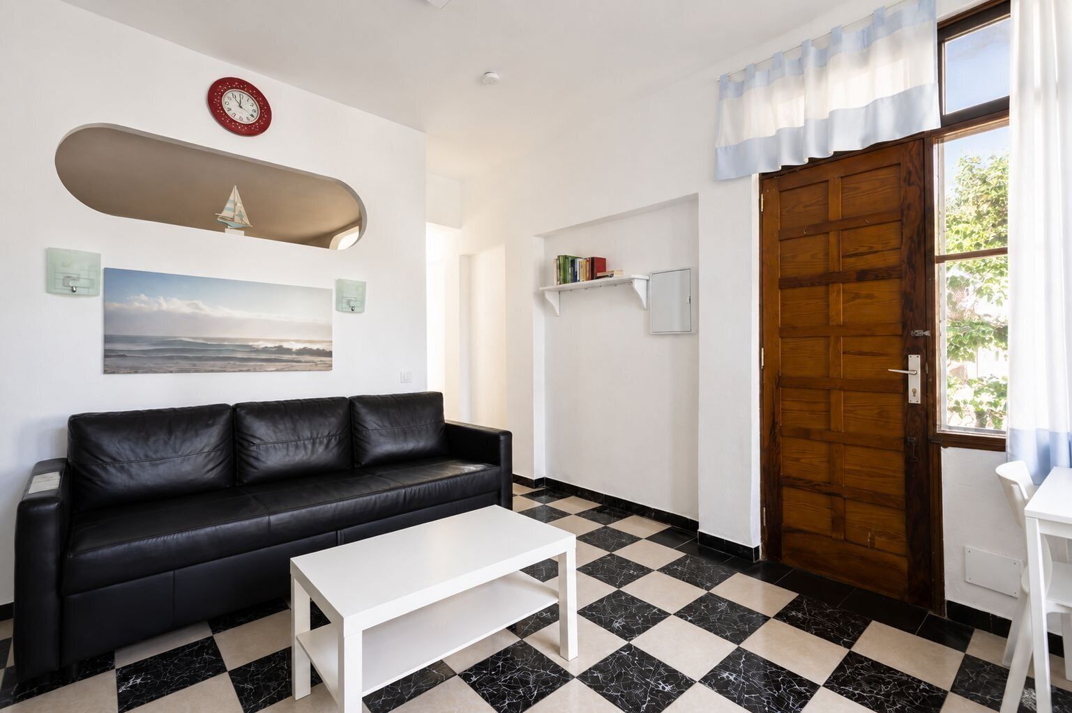 A room with a black leather sofa, a white coffee table, a wooden door, and a checkered floor.