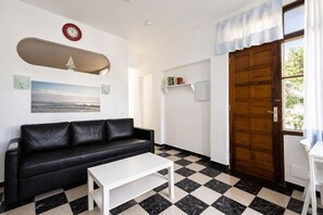 A room with a black leather sofa, a white coffee table, a wooden door, and a checkered floor. - GuestReady - San Agustin Pool Escape (Playa del Ingles)
