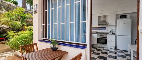A patio with a wooden table and chairs, a potted plant, and a window with blue curtains.