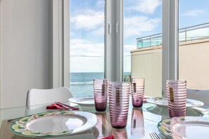 A dining table with plates and glasses, a white chair, and a view of the ocean through large windows. - GuestReady - Sunset Canteras Sea Views (Las Palmas de Gran Canaria)