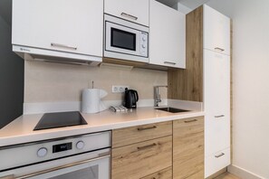 A modern kitchen with white cabinets, a built-in microwave, a stove, and a coffee maker. - GuestReady - Sunset Canteras Sea Views (Las Palmas de Gran Canaria)