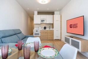 Una habitación de hotel moderna con zona de comedor, kitchenette y un televisor que muestra 'GUEST READY'.