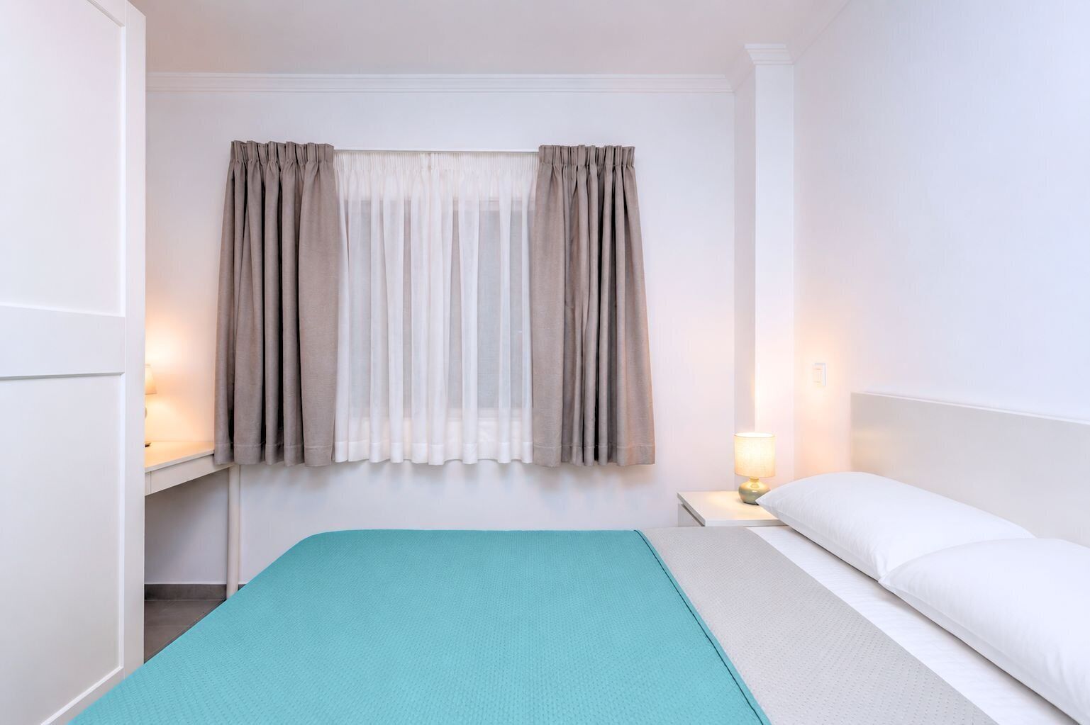 A hotel room with a bed, a nightstand with a lamp, and a window with curtains.