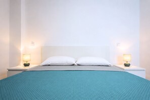 Ein Bett mit zwei weißen Kissen, einer türkisblauen Tagesdecke und zwei Nachttischlampen auf weißen Nachttischen.