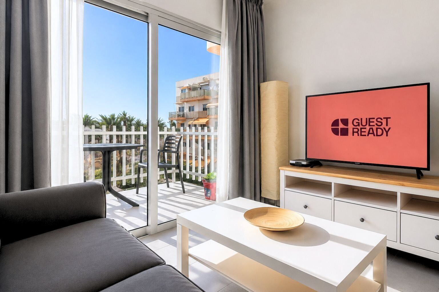 Ein modernes Hotelzimmer mit Balkon, Flachbildfernseher, Sofa, Esstisch und einer Holtschale.