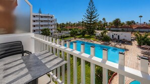 Un balcón con vistas a una piscina, un comedor y un edificio de varios pisos.
