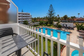 Ein Balkon mit Blick auf einen Swimmingpool, einen Essbereich und ein mehrgeschossiges Gebäude.