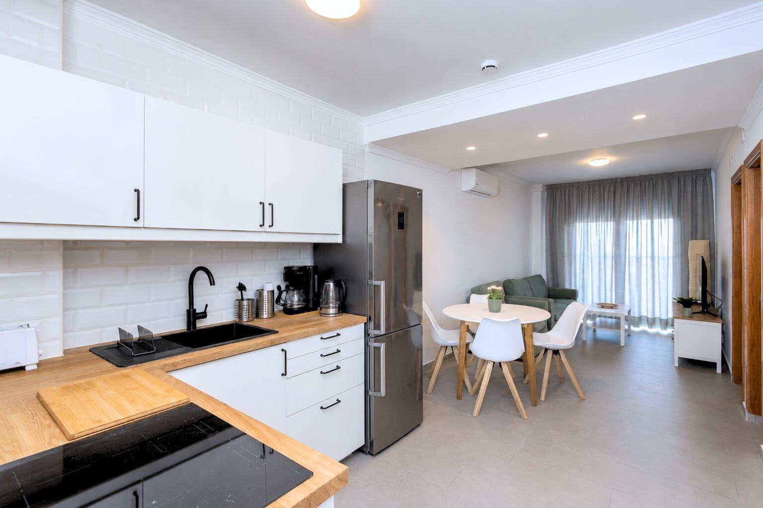 Una cocina moderna con armarios blancos, un refrigerador de acero inoxidable y un comedor con una mesa redonda y sillas.