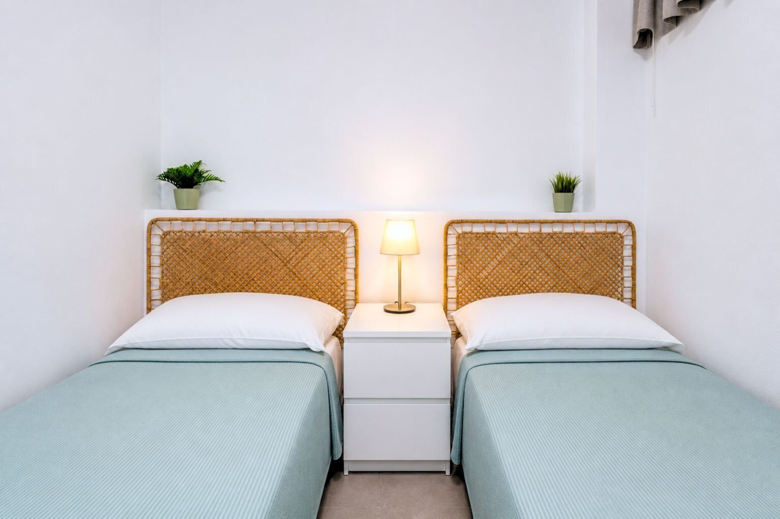 Ein Doppelzimmer mit zwei Betten, einem Nachttisch mit Lampe und zwei kleinen Topfpflanzen.