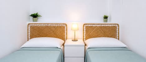 Habitación doble con dos camas, una mesita de noche con lámpara y dos pequeñas macetas.