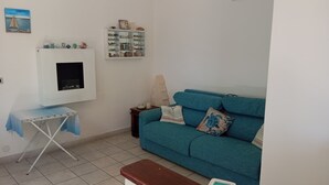 A living room with a teal sofa, a small table, a cabinet with decorative items, and a wall-mounted TV.