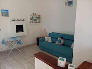 Una sala de estar con un sofá azul turquesa, una mesita, un aparador con adornos y un televisor montado en la pared.