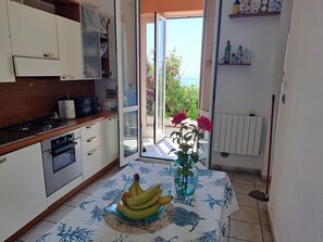 A kitchen with a stove, oven, and a table with a vase and bananas. - Orizzonte Blu Giardino sul Mare, Finale Ligure, on the beachfront (Finale Ligure)