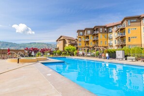 Et hotel med swimmingpool, flere balkoner og et bjerglandskab i baggrunden.