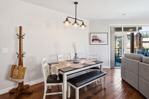Een eetruimte met een tafel, stoelen, een bank, een kapstok, een hanglamp en een ingelijste foto aan de muur.