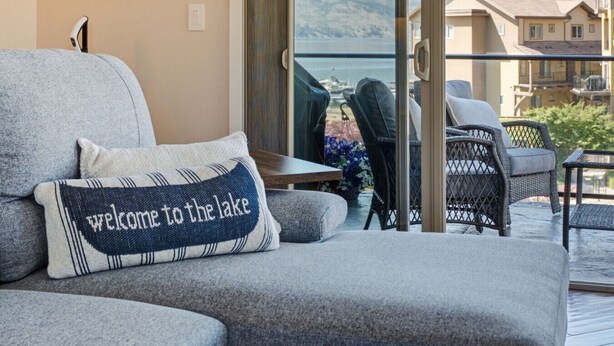 A balcony with a sofa, a table, and chairs, overlooking a lake and mountains. - 3BR Condo | Lake & Pool Views | Beach Resort (West Kelowna)