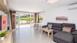 A modern living room with a grey sofa, a coffee table, and a TV on the wall. - GuestReady - Sun Club Hammock Relax (San Bartolomé de Tirajana)