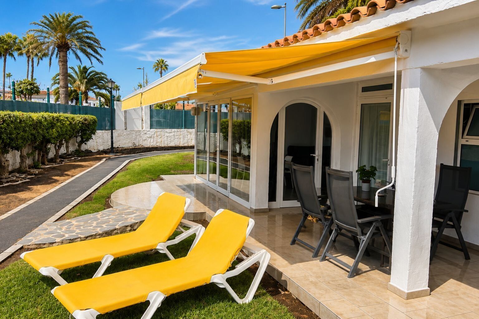 A patio with yellow lounge chairs, a table with chairs, and a glass enclosure.