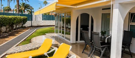A patio with yellow lounge chairs, a table with chairs, and a glass enclosure.