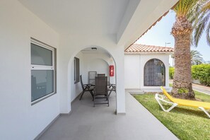 A covered outdoor area with a table and chairs, a yellow lounge chair, and a palm tree. - GuestReady - Sun Club Hammock Relax (San Bartolomé de Tirajana)