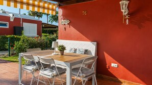 A patio with a wooden table and white chairs, a red wall with the number 76, and a small potted plant. - GuestReady - Los Tunos Family Pool (Maspalomas)