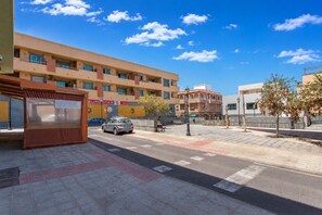 A street view with a row of buildings, a parked car, and a pedestrian walkway. - GuestReady - Stylish Retreat Steps from the Beach (Corralejo)