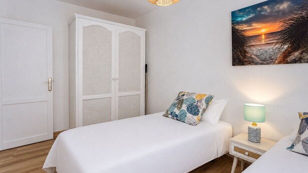 Quarto com cama, mesa de cabeceira, luminária, guarda-roupa e pintura de um pôr do sol.