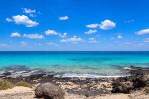 Una playa con agua turquesa cristalina, costa rocosa y cielo despejado.