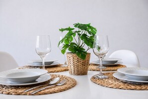 A table set with plates, cutlery, and two wine glasses, with a woven placemat and a potted plant in the center. - GuestReady - Stylish Retreat Steps from the Beach (Corralejo)