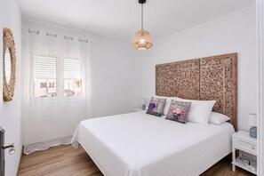 Un dormitorio con una cama grande, un cabecero decorativo, una ventana con persianas y una lámpara colgante.