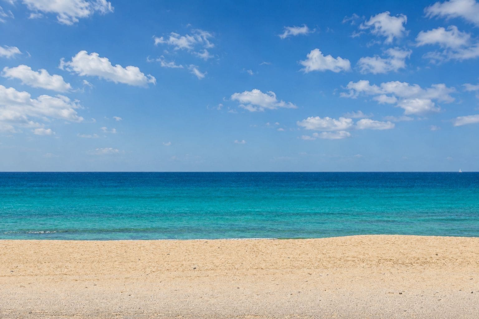 A beach with clear blue water and a sandy shore.