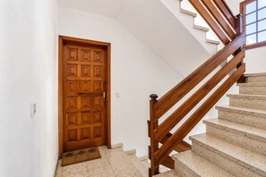 A wooden door with a textured surface, a wooden staircase with a handrail, and a doormat on the floor. - GuestReady - Stylish Retreat Steps from the Beach (Corralejo)