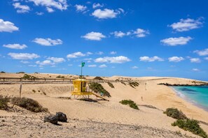 Ein Strand mit einem Rettungsturm, Sanddünen und einem wolkenlosen, blauen Himmel.