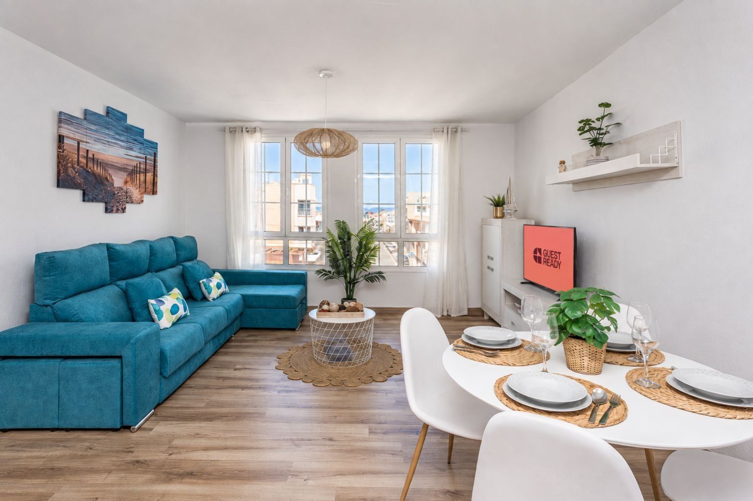 A modern living room with a teal sofa, a dining table set for four, and a large window with a view.
