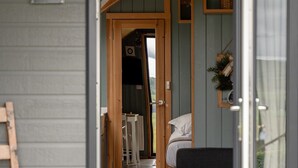 A cozy interior with a wooden door leading to a room with a bed, a chair, and a small table. - Greendale Glamping - Sunrise Pod (No Hot Tub) (Chatburn)