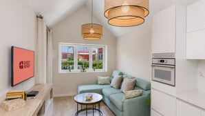 Una sala de estar moderna con un sofá verde, una mesa de centro, un televisor y una zona de cocina con horno.