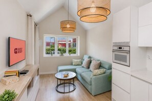A modern living room with a green sofa, a coffee table, a TV, and a kitchen area with an oven. - GuestReady - Los Tunos Barbecue and Pool (Maspalomas)