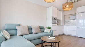 Una sala de estar moderna con sofá, una mesa de centro y una cocina con electrodomésticos.