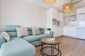 A modern living room with a sofa, a coffee table, and a kitchen area with appliances. - GuestReady - Los Tunos Barbecue and Pool (Maspalomas)