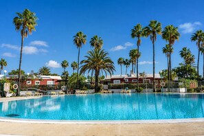A swimming pool surrounded by palm trees and red buildings. - GuestReady - Los Tunos Barbecue and Pool (Maspalomas)