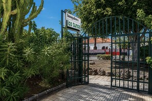 Un cancello con un cartello che indica 'bungalows los tinos' e vista su un edificio con tetto in tegole rosse.