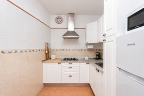A compact kitchen with white cabinets, a gas stove, a coffee maker, and a Brandt refrigerator.