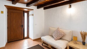 Ein Zimmer mit Holztür, einem Sofa mit einem Blumenkissen, einem kleinen Tisch mit einer Lampe und einer Vase mit getrockneten Pflanzen.