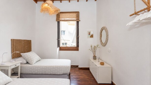Ein Schlafzimmer mit zwei Betten, einem Schreibtisch, einer Kommode, einer Pendelleuchte, einem Fenster und einem Spiegel an der Wand.