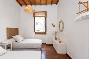 A bedroom with two beds, a desk, a dresser, a hanging light fixture, a window, and a mirror on the wall.