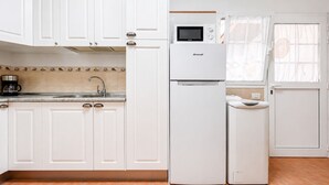 Eine Küche mit weißen Schränken, einer Brandt-Mikrowelle, einer Kaffeemaschine und einem Kühlschrank.