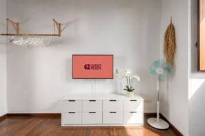Ein Hotelzimmer mit einer weißen Kommode, einem Flachbildfernseher, einem Standventilator und einer Zierpflanze.